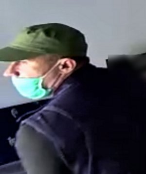 Na zdjęciu widoczna twarz mężczyzny, który ma na głowie czapkę z daszkiem koloru zielonego, na twarzy ma założona maseczkę. Mężczyzna jest w bluzce koloru granatowego.