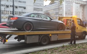 Na zdjęciu widoczne poszukiwane auto marki BMW znajdujące się na lawecie. Obok stoi umundurowany policjant.