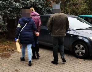 Na zdjęciu widoczni nieumundurowani policjanci wraz z zatrzymaną kobieta, którą prowadzą do radiowozu.