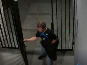 Na zdjęciu jest widoczny mężczyzna trzymający drzwi wejściowe na osiedle, ubrany w czarna koszulkę z krótkim rękawem i spodnie jeansowe długie.