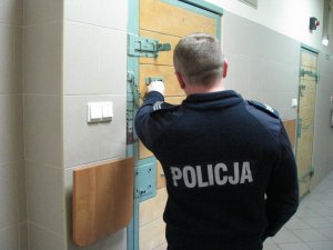 Na zdjęciu umundurowany policjant w pomieszczeniu, gdzie znajdują się pokoje dla zatrzymanych.