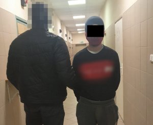 Na zdjęciu widoczny nieumundurowany policjant, który trzy ma za rękę zatrzymanego mężczyznę.
