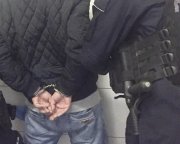 Na zdjęciu zatrzymany mężczyzna trzymany za ręce przez umundurowanego policjanta.
