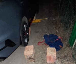 Na zdjęciu widoczny pojazd kia w kolorze niebieskim, obok leżące pustaki, torba podróżna i lewarek znajdujący się pod kołem.