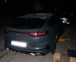 Na zdjęciu widoczny pojazd kia w kolorze niebieskim, obok leżące pustaki, torba podróżna i lewarek znajdujący się pod kołem.