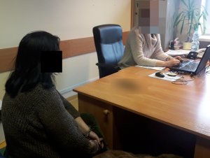 Na zdjęciu widoczna nieumundurowana policjantka, przy jej biurku siedzi na krześle zatrzymana kobieta.