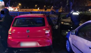 Na zdjęciu widoczny umundurowany policjant który trzyma za rękę zatrzymanego mężczyznę, obok przy pojedzie koloru czerwonego stoi drugi zatrzymany mężczyzna.