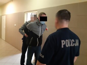Na zdjęciu widoczny zatrzymany mężczyzna , któremu na ręce zakłada kajdanki nieumundurowany policjant.