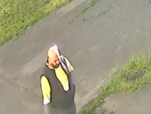 Na zdjęciu widoczny mężczyzna, ma koszulkę z krótkim rękawem w kolorze żółtym, nałożona granatową pikowaną kamizelkę, spodnie typu jeans, na twarzy ma brodę, jest łysy.