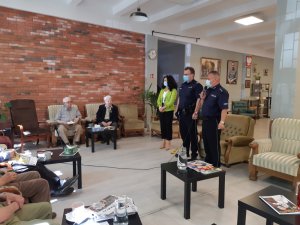 Na zdjęciu widocznych dwóch umundurowanych policjantów w pomieszczeniu domu wsparcia. Na fotelach siedzą powstańcy.