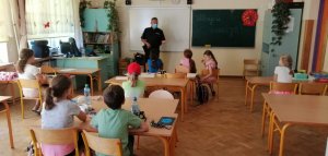 Na zdjęciu widoczny umundurowany policjant wraz z dziećmi w pomieszczeniu szkolnym.