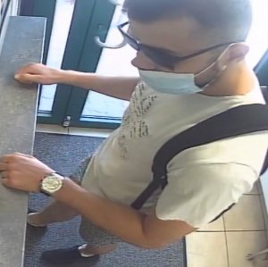 Na zdjęciu widoczny mężczyzna, ma czarne okulary, koszulkę białą z krótkim rękawem, na plecach czarny plecak.