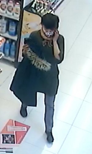 Na zdjęciu widoczna kobieta, która trzyma w ręku płaszcz koloru ciemnego, na twarzy ma założoną maseczkę białą w czarne kropki.