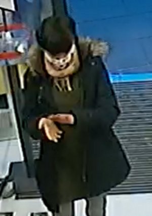 Na zdjęciu widoczna kobieta, która ma założony płaszcz koloru ciemnego, na twarzy ma założoną maseczkę białą w czarne kropki.