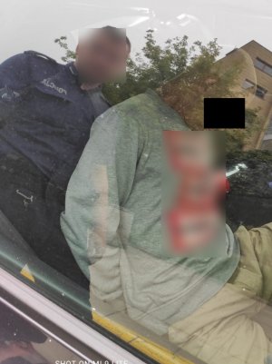 Na zdjęciu widoczny zatrzymany mężczyzna, który siedzi w pojeździe, obok stoi  umundurowany policjant.