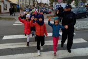 Na zdjęciu widoczny umundurowany policjant przechodzący przez przejście dla pieszych wraz z dziećmi.