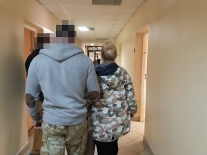 Na zdjęciu widoczny nieumundurowany policjant, który prowadzi zatrzymaną kobietę