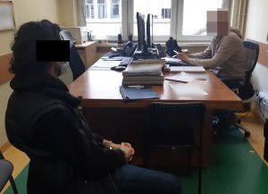 Na zdjęciu widoczny nieumundurowany policjant, na krześle siedzi zatrzymany mężczyzna.
