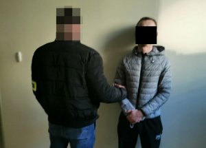 Na zdjęciu widoczny nieumundurowany policjant, który trzyma za rękę zatrzymanego mężczyznę.