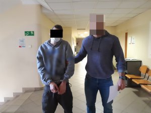 Na zdjęciu widoczny nieumundurowany policjant, który trzyma za rękę zatrzymanego mężczyznę.