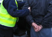 Na zdjęciu widoczny umundurowany policjant, który prowadzi zatrzymanego mężczyznę.