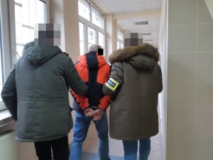 Na zdjęciu widoczni nieumundurowani policjanci, którzy prowadzą zatrzymanego mężczyznę.