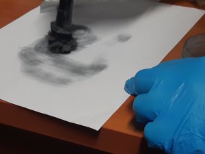Na zdjęciu technik, który zbiera ślady daktyloskopijne z kartki papieru.