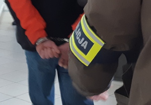 Na zdjęciu widoczny policjant, który zakłada kajdanki zatrzymanemu mężczyźnie.