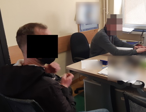 Na zdjęciu widoczny nieumundurowany policjant, obok siedzi na krześle zatrzymany mężczyzna.