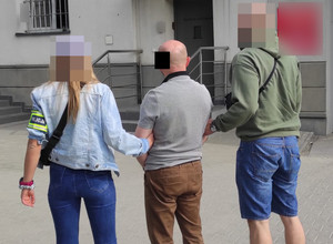 Na zdjęciu widoczni nieumundurowani policjanci i zatrzymany mężczyzna.