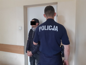 Na zdjęciu widoczny umundurowany policjant i zatrzymany mężczyzna.