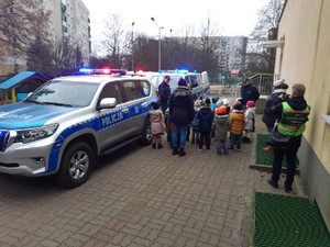 Na zdjęciu widoczne dzieci w radiowozie obok stojący umundurowani policjanci.