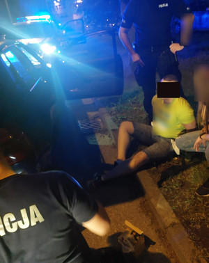 Na zdjęciu widać policjantów i siedzącego na ziemi zatrzymanego mężczyznę.