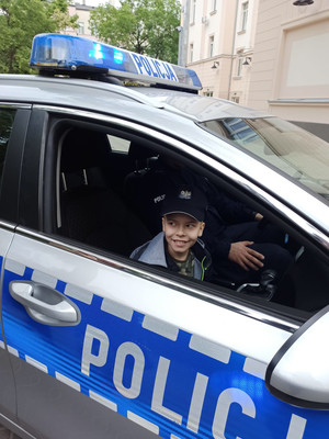 Na zdjęciu widać policyjny radiowóz i chłopca siedzącego na przednim fotelu.