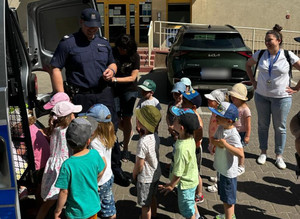 Dzieci stojące przy oznakowanym radiowozie z policjantem.
