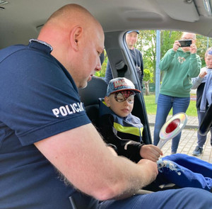Policjanci umundurowany z chłopcem w radiowozie.
