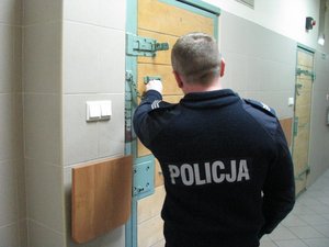 Policjant zamykający drzwi od pomieszczenia dla osób zatrzymanych.