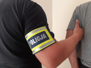 Policjant trzymający za rękę zatrzymanego.