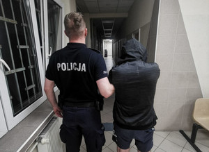 Policjant trzyma za rękę zatrzymanego.