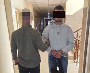 Policjant trzyma za rękę zatrzymanego.